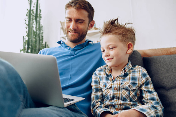 Father and son sitting on couch and watching something on laptop - Foto, Imagem