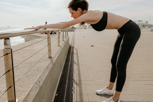 Donna sportiva e felice che si estende parte superiore del corpo dopo aver fatto jogging, in posa all'aperto. - Foto, immagini