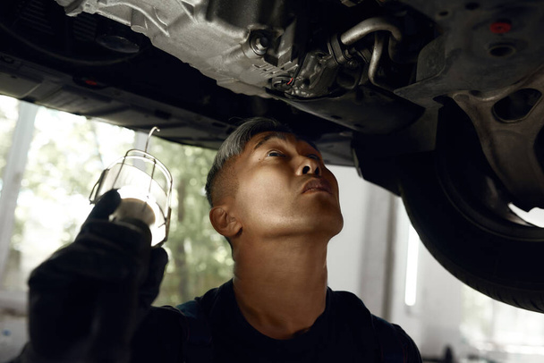 Mechanic looking up at auto bottom lightened by flashlight - Fotoğraf, Görsel