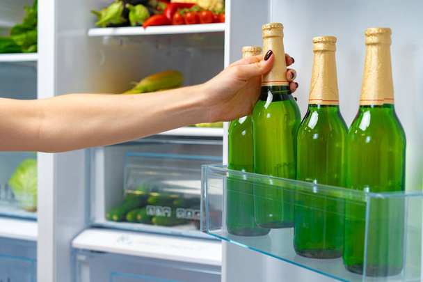 Female hand taking bottle of beer from a fridge - Foto, afbeelding