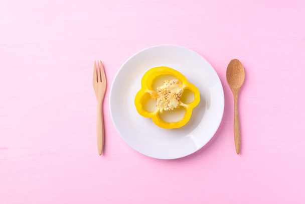 Sliced yellow bell pepper on white plate with wooden fork and spoon on pink background, Top view - Foto, Imagen