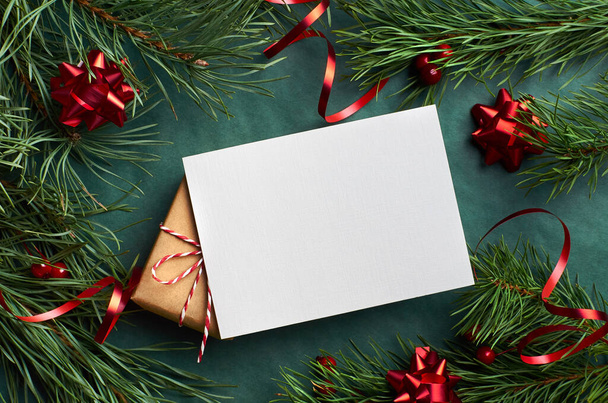 Christmas greeting card mockup with gift box, pine tree branches and festive red tape on green background - Photo, Image