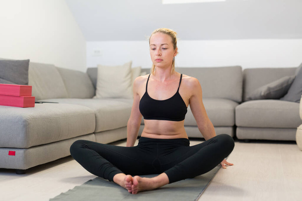 Beautiful blonde woman doing home workout indoors. Woman practice yoga at home. Fit girl using workout tutorials for healthy active lifestyle. Woman using quarantine for home workouts. - Foto, imagen