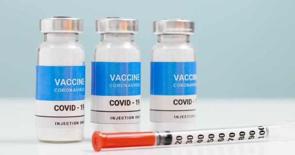 Coronovirus, vacuna covid-19 de la población. Viales de vacunas y jeringa sobre una mesa blanca de laboratorio con espacio para copias. Concepto de cura sanitaria - Metraje, vídeo