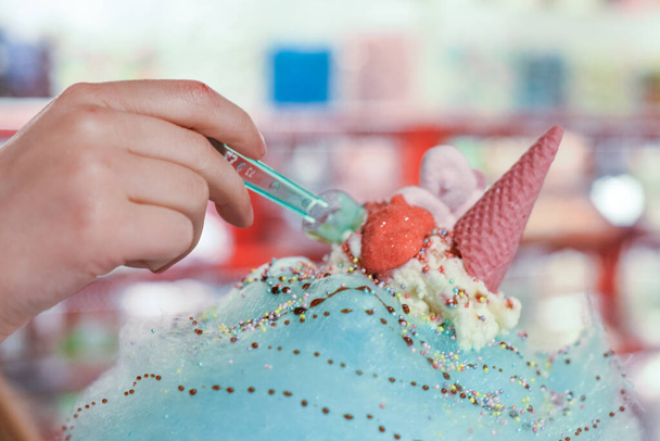 Παιδί τρώει γλυκά και καραμέλες σε ένα τεράστιο βαμβακερό νήμα καραμέλα με παγωτό και σάλτσα επιδόρπιο - Φωτογραφία, εικόνα