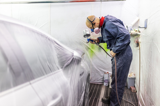 young adult male car painter, painting a car in the paint booth of his workshop - Foto, imagen