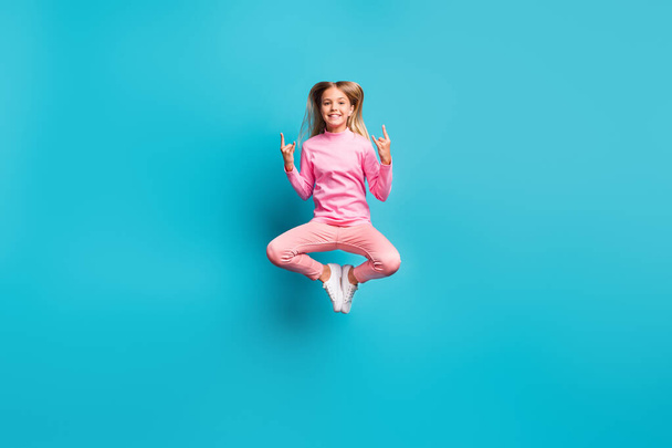 Full size photo of careless positive blond hair girl jump show rock sign wear pink pants poloneck white footwear isolated on teal background - Zdjęcie, obraz