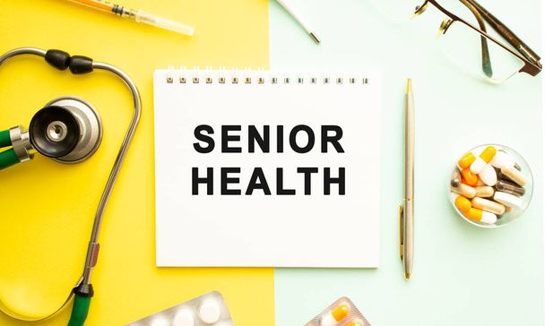 Text SENIOR HEALTH on notebook with stethoscope and pen on yellow background. Medical concept. - Photo, Image