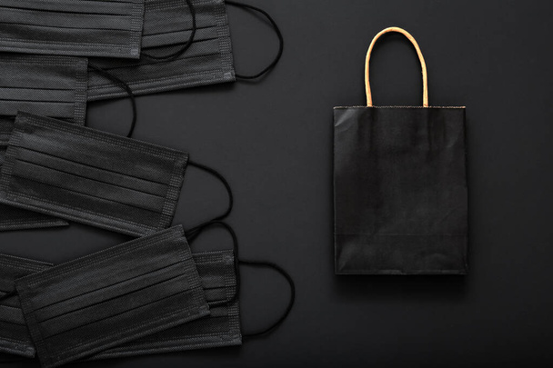 Shopping paper bag with black medical face masks. Shopping, Food delivery in covid 19 lockdown quarantine. Black Friday cyber Monday sale concept. Online shopping on dark black background. Mock up - Photo, image
