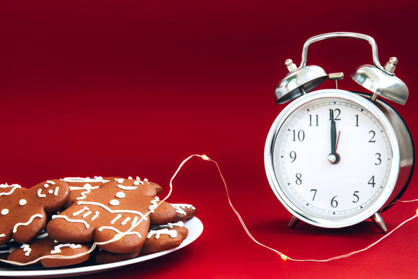 Relógio de alarme de prata vintage bonito e placa de biscoitos de gengibre em um fundo vermelho brilhante. Conceito de tempo. Rotina de férias - Foto, Imagem