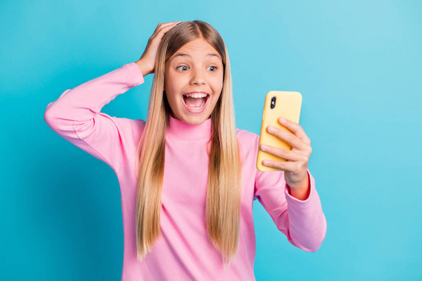 Photo portrait of shocked surprised female preteen looking at smartphone with opened mouth isolated on vibrant teal color background - 写真・画像