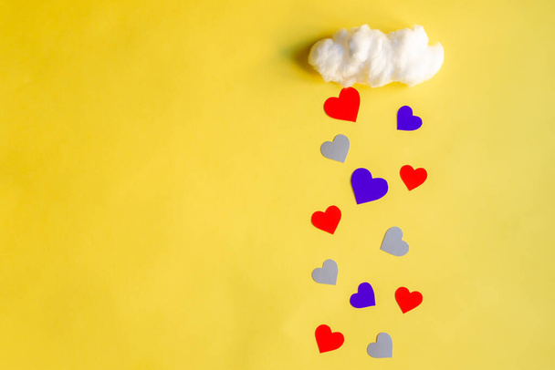 Colorful hearts rain from white cotton cloud on a yellow background, with copy space. Valentine's day, love and wedding concept, flat lay - Photo, Image