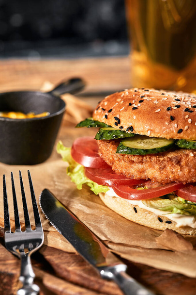 Das Konzept des amerikanischen Fast Food. Ein saftiger amerikanischer Burger mit zwei Rindfleischpasteten und einem dunklen Bier auf einem Glastisch und orangefarbenem Hintergrund. Kopierraum - Foto, Bild