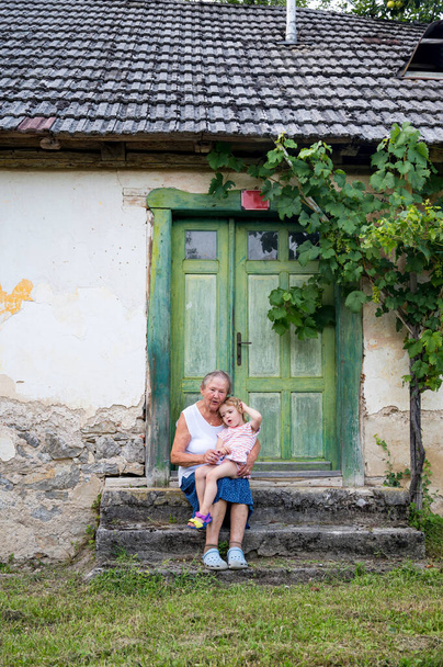 Avó sentada com sua avó na frente de sua antiga casa. - Foto, Imagem