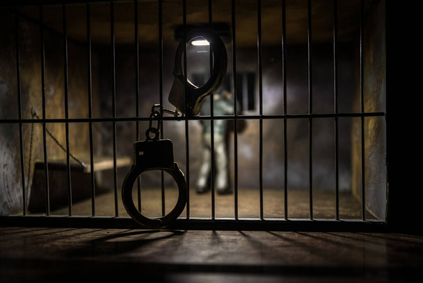 Hapisteki adam demir parmaklıklar arkasında. Eski edepsiz hapishane minyatürü. Karanlık hapishane iç dekorasyonu, kelepçeli. Seçici odak - Fotoğraf, Görsel