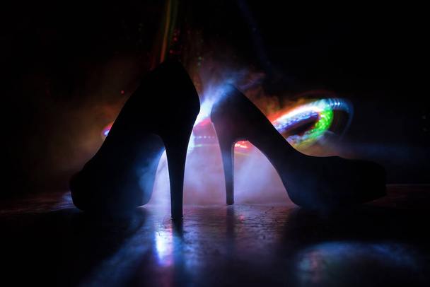 Διακόσμηση έργων τέχνης. Σιλουέτα από ψηλοτάκουνα γυναικεία παπούτσια στο σκοτάδι. Γυναικεία εξουσία ή γυναικεία κυριαρχία έννοια. Επιλεκτική εστίαση - Φωτογραφία, εικόνα