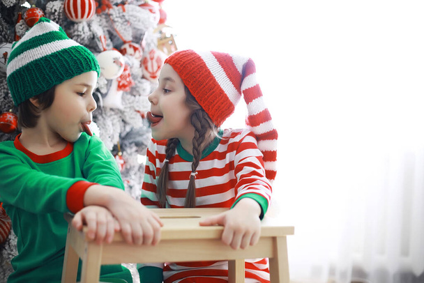 Noel Baba 'nın yardımcıları. Noel' de Noel için dekore edilmiş bir odada elf kostümleri giymiş şirin çocuklar. Mucizeler zamanı. Noel Baba 'dan hediyeler - Fotoğraf, Görsel