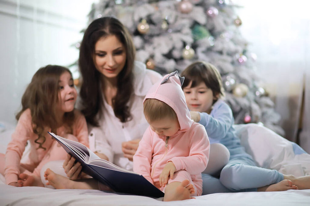 Μια οικογένεια με παιδιά που διασκεδάζουν στο κρεβάτι κάτω από τα σκεπάσματα κατά τη διάρκεια των Χριστουγέννων. - Φωτογραφία, εικόνα