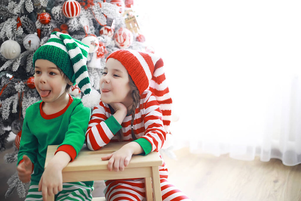 サンタクロースのヘルパークリスマスのために美しく装飾された部屋でクリスマスの自己の衣装でかわいい子供たち。奇跡の時だ。サンタクロースからの贈り物 - 写真・画像