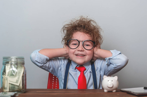 Young businessman does not know what to do in crisis so he closed his ears. financial education concept. Child in glasses and suit with piggy bank and jar full of money. Investment concept - Φωτογραφία, εικόνα
