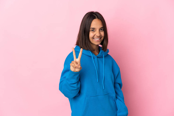 Young latin woman isolated on pink background smiling and showing victory sign - Photo, Image