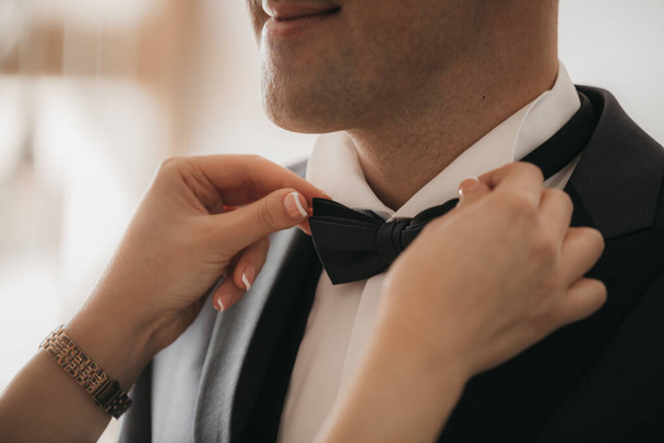 A selective focus closeup of a female's hand buttoning the groom's bowtie - Foto, Imagen