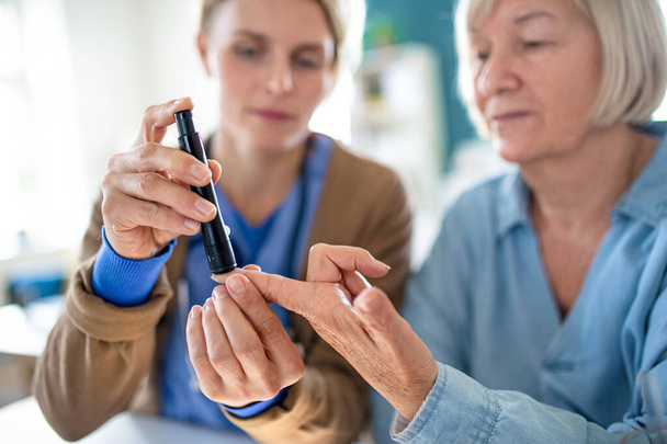 Caregiver or healthcare worker with senior woman patient, measuring blood glucose indoors. - Foto, imagen