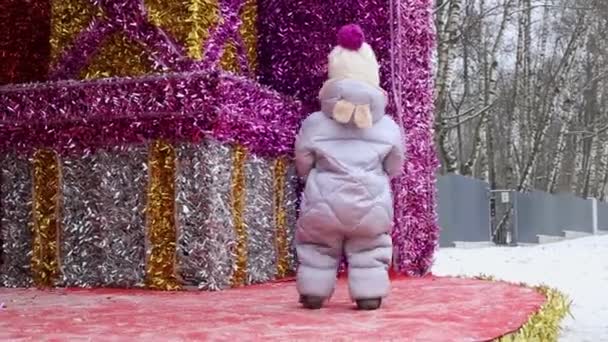 Un enfant en combinaison d'hiver marche sur une scène décorée dans la rue dans le parc en hiver - Séquence, vidéo