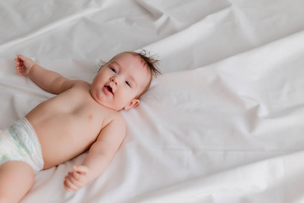 χαριτωμένο μωρό ξαπλωμένο στο κρεβάτι με λευκά σεντόνια - Φωτογραφία, εικόνα