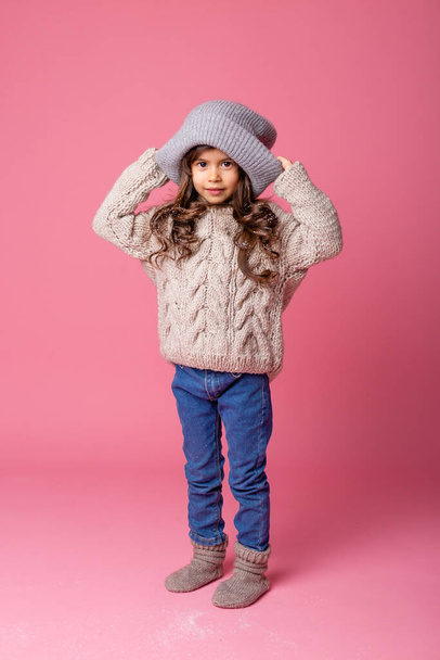 klein meisje dragen warme kleren staan op roze achtergrond - Foto, afbeelding