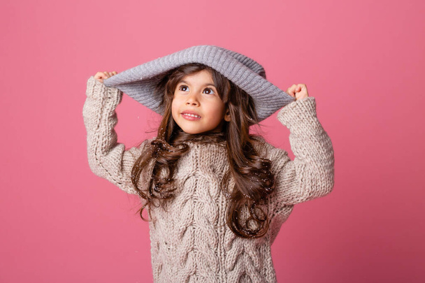 ピンクの背景に大きな暖かい帽子をかぶった女の子 - 写真・画像