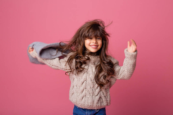 klein meisje het nemen van warme hoed af op roze achtergrond - Foto, afbeelding