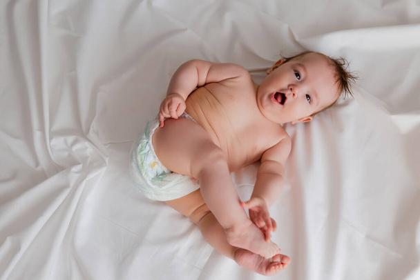bovenaanzicht van schattige baby liggend op witte lakens - Foto, afbeelding