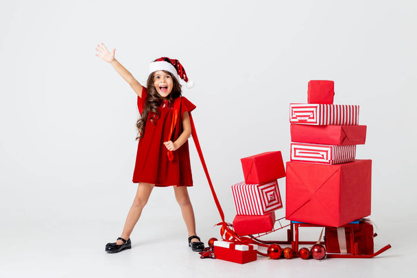 мила дівчина в капелюсі Санта, що несе санчата з багатьма подарунками
 - Фото, зображення
