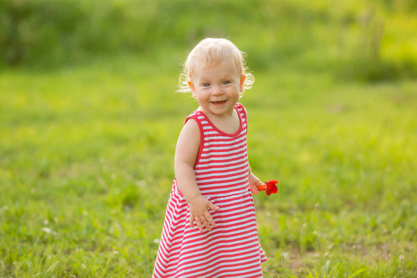χαμογελαστό κοριτσάκι φορώντας κόκκινο ριγέ φόρεμα εκμετάλλευση λουλούδι - Φωτογραφία, εικόνα
