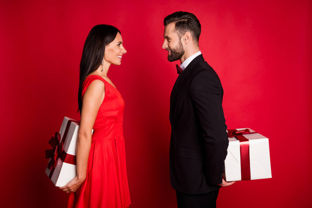 Profile photo of cute optimistic couple hide presents wear suit dress isolated on red color background - Fotó, kép