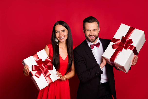 Photo of two positive persons holding x-mas giftbox toothy smile isolated on red color background - Fotoğraf, Görsel