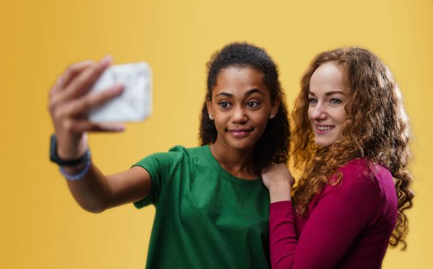 Young woman with teenager girl in a studio on yellow background, taking selfie. - Foto, Imagen