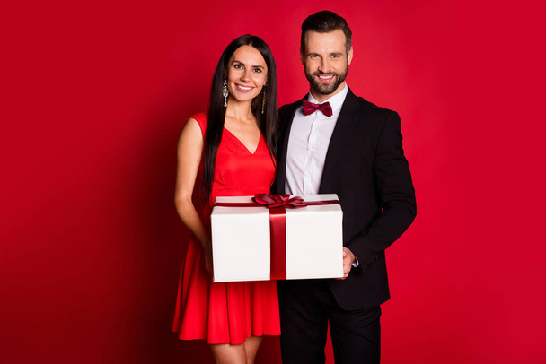 Photo of nice optimistic couple hold gift wear suit dress isolated on red color background - Fotó, kép