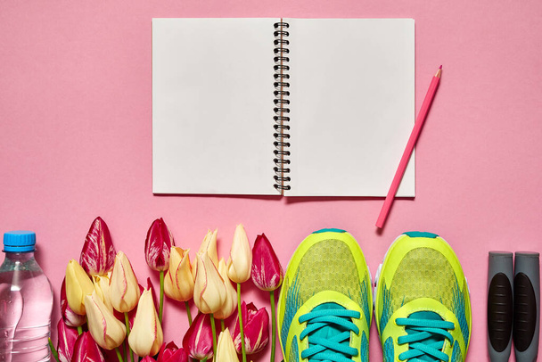 Spring sport composition with running shoes, red and yellow tulips and open blank notebook on pink background, copy space. Sports concept. Top view, flat lay - Fotografie, Obrázek