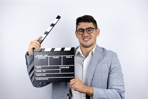 Business young man wearing a casual shirt over white background holding clapperboard very happy having fun - Photo, Image