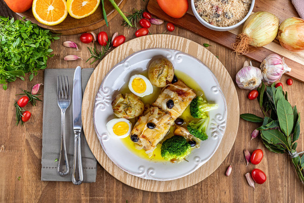 Cod loin baked in olive oil, with potatoes, broccoli, boiled egg and black olives. Typical dish of Portugal. Top view. Space for text. - Photo, Image