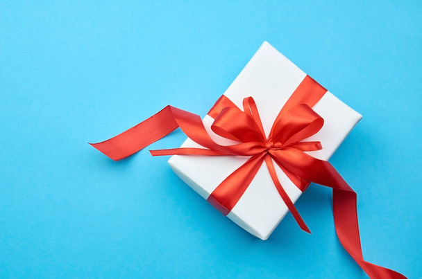 White gift box with red ribbon bow on blue background - Zdjęcie, obraz