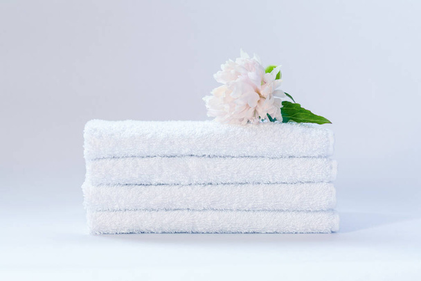 Cuatro toallas blancas de rizo cuidadosamente dobladas con una flor de peonía delicadamente rosa sobre un fondo claro - Foto, imagen