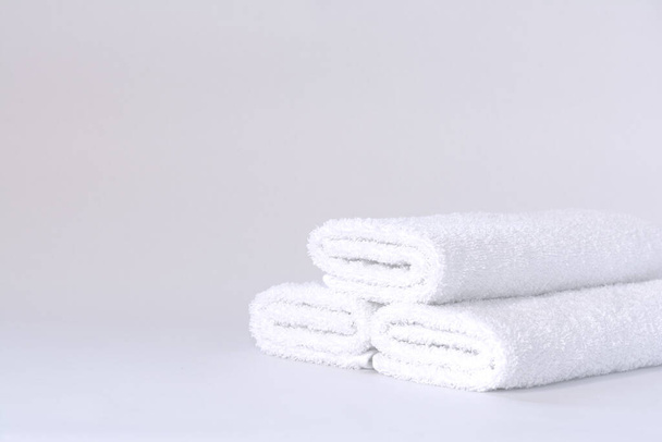 Trzy białe starannie złożone ręczniki frotte na jasnym tle - Zdjęcie, obraz