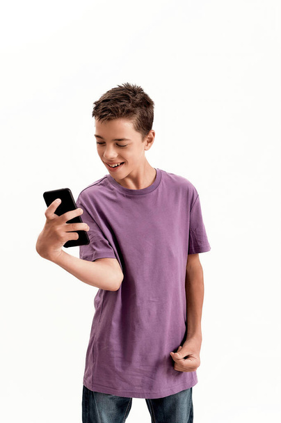Teenaged disabled boy with cerebral palsy looking happy while holding and using smartphone, posing isolated over white background - Photo, Image