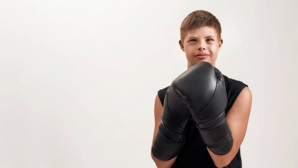 Portrait of cheerful disabled boy with Down syndrome wearing big boxing gloves, looking at camera while posing isolated over white background - Fotó, kép