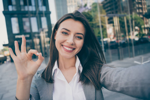 Photo of joyful pretty businesswoman wear formalwear suit jacket make selfie okay sign in outdoors center - Photo, Image
