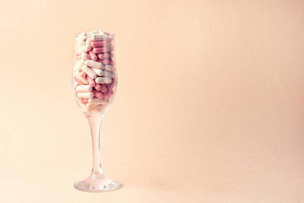 Šamanská sklenice je plná bílých a růžových pilulek. Koncept dovolené v podmínkách nemoci. Kopírovat mezeru na růžovém pozadí - Fotografie, Obrázek