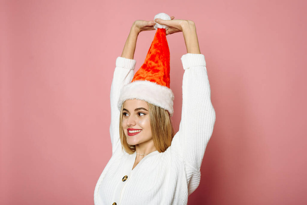 Noel Baba şapkasından bir ponpon tutan ve pembe arka planda kameraya bakan komik kadın. Gülümseyen mutlu kadın - Fotoğraf, Görsel